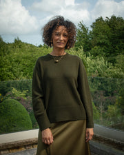 Woman wearing a green sweater and skirt standing outdoors with trees in the background Alnwick Northumberland