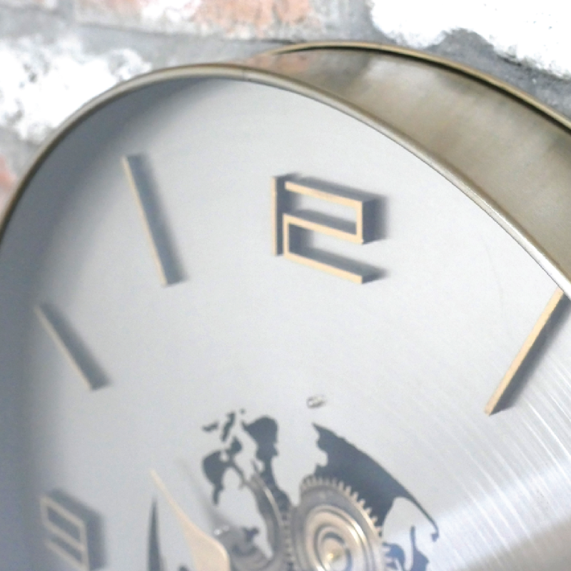 Decorative wall clock featuring a world map design, silver background, gold numerals, and functional cog details, dimensions 60cm H × 60cm W × 8cm D, weight 5kg.